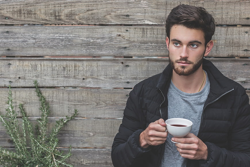 Young Man Holding Coffee Cup Against Wooden Wall