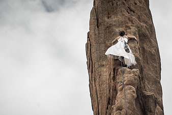 Woman in white dress climbing a tall rock formation