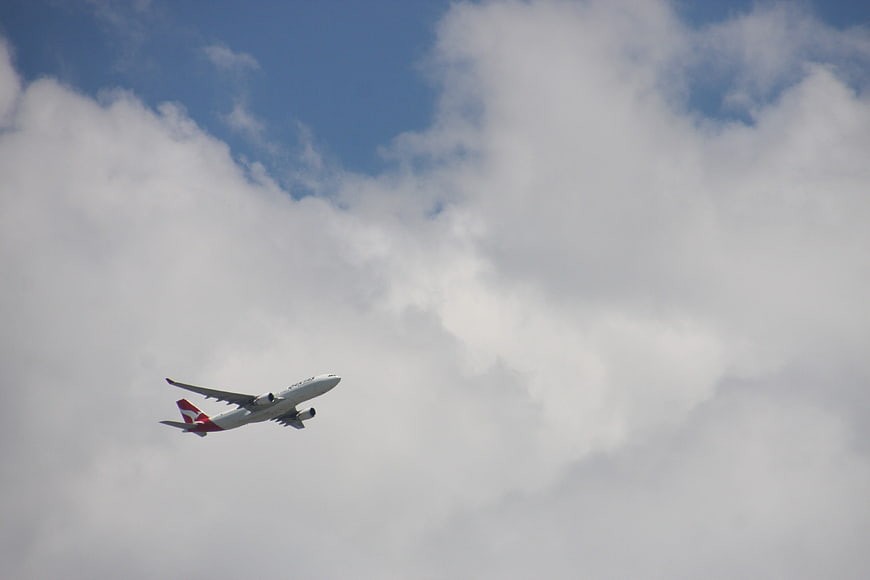 Qantas airplane ascending into cloudy blue sky