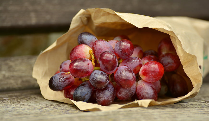 Fresh red grapes spilling from a brown paper bag on a rustic wooden table