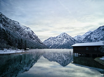 Serene Winter Lake with Snowy Mountains and Wooden Boathouse