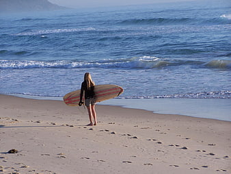 Female Surfer Standing on Sandy Beach with Surfboard