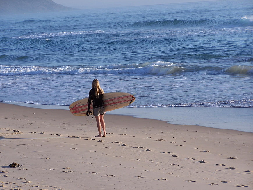 Female Surfer Standing on Sandy Beach with Surfboard