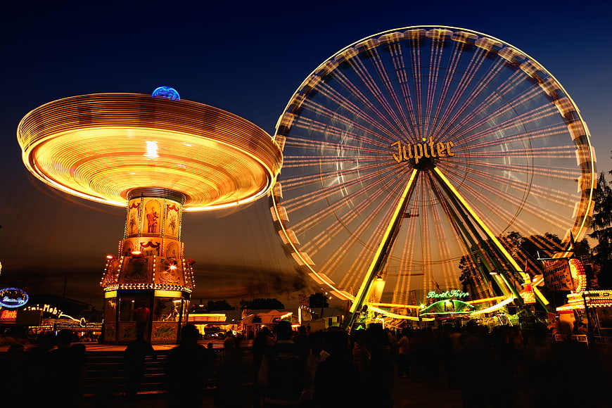 Night shot of illuminated Ferris wheel and spinning fairground ride