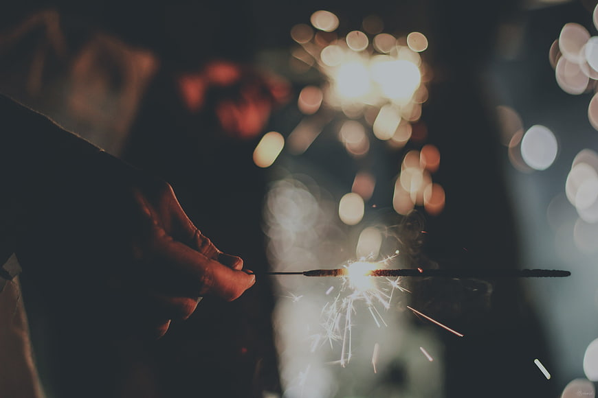 Hand holding a lit sparkler with bokeh lights
