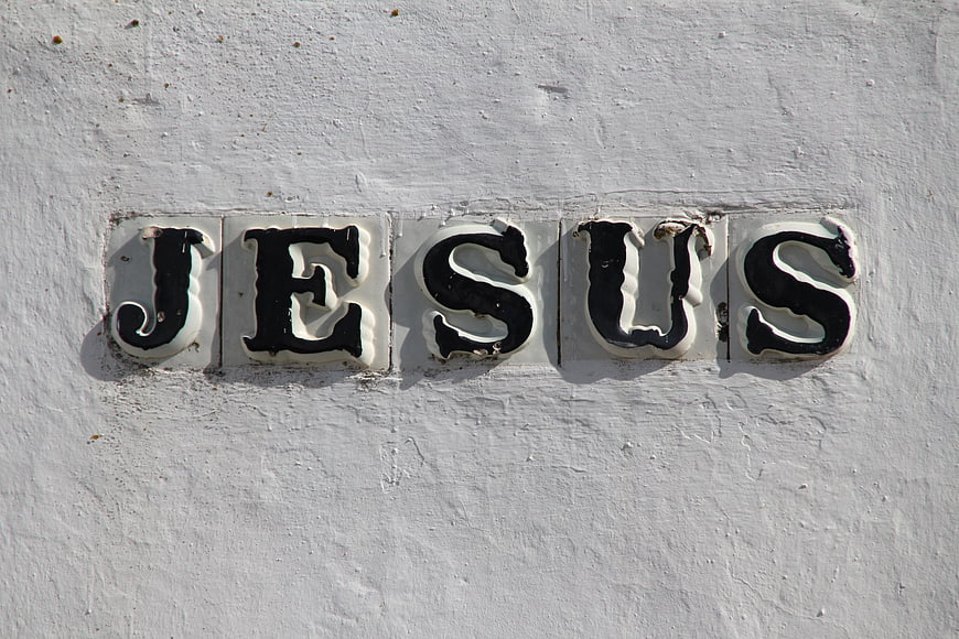 Ceramic tiles spelling Jesus on a white textured wall