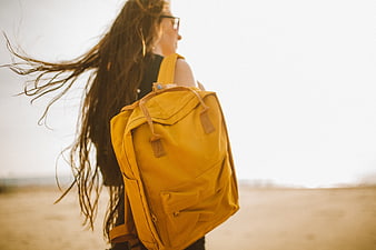 Woman with yellow backpack walking on beach