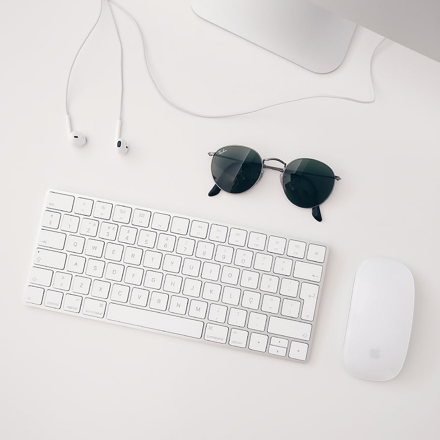Minimalist white workspace with keyboard, mouse, sunglasses, and earphones