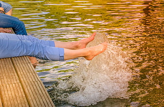 Woman splashing feet in pond water from wooden dock