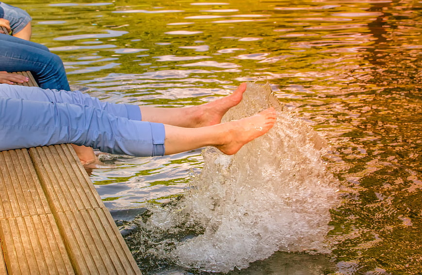 Woman splashing feet in pond water from wooden dock