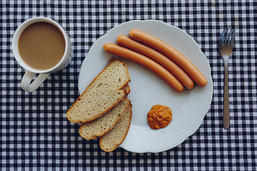 Overhead view of breakfast sausages, bread, and coffee on checkered tablecloth