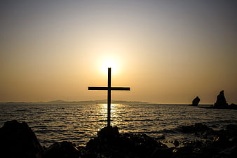 Silhouette of Cross on Rocky Shore at Sunset