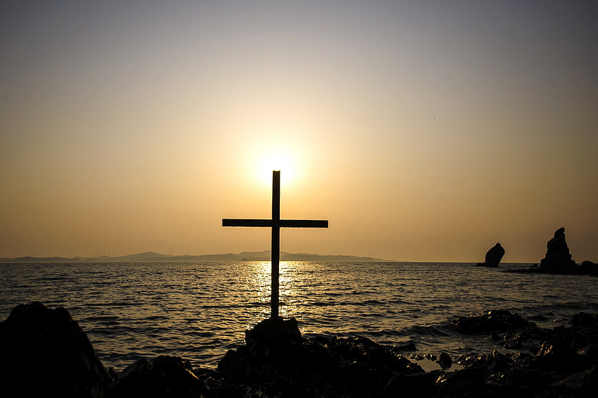 Silhouette of Cross on Rocky Shore at Sunset