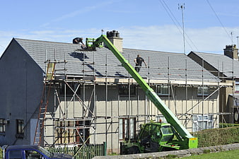 Workers repairing roof with green cherry picker and scaffolding