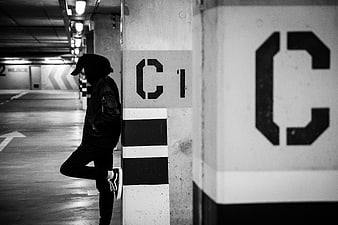 Man in Hoodie Leaning Against Concrete Pillar in Parking Garage