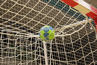 Green and blue handball stuck in white goal net