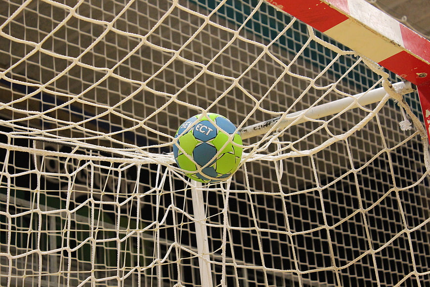 Green and blue handball stuck in white goal net