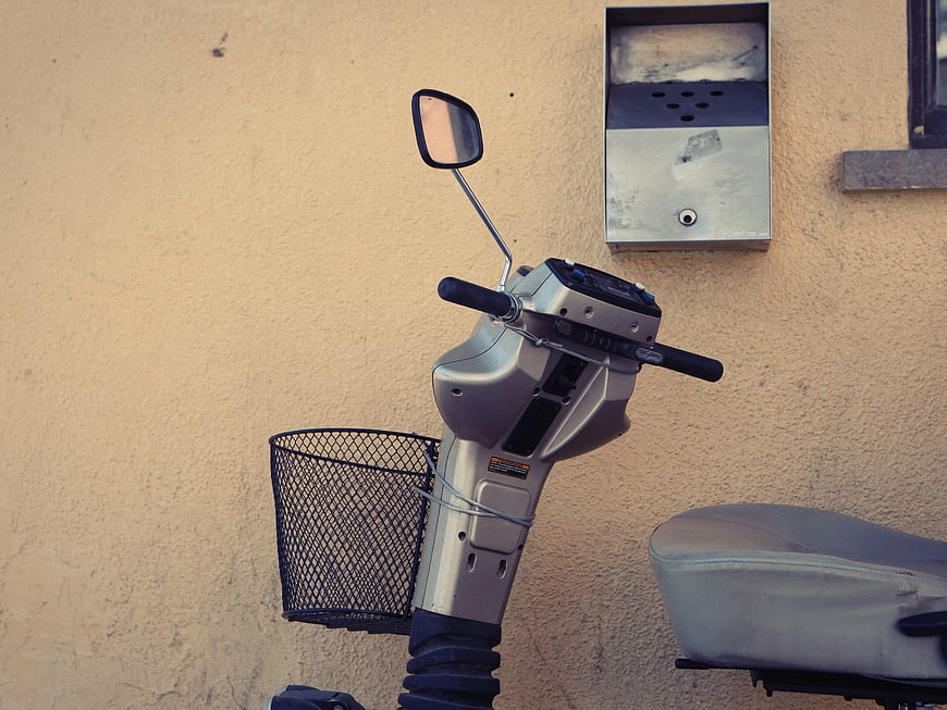 Silver motorized scooter parked against beige wall