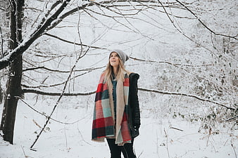 Woman in plaid blanket standing in snowy winter forest