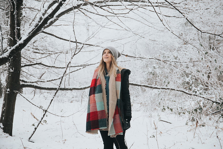 Woman in plaid blanket standing in snowy winter forest