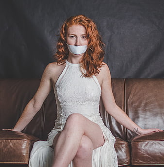 Redhead woman with white tape over mouth sitting on leather sofa