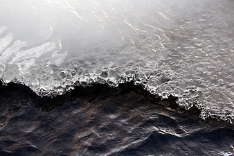 Close-up of frozen ice edge meeting dark river water