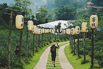 Woman in Conical Hat Walking Under Lantern Archway