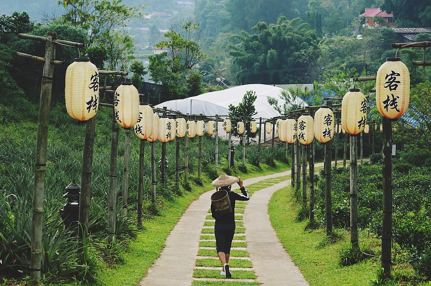 Woman in Conical Hat Walking Under Lantern Archway