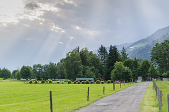 Sunbeams over green meadow and gravel road in mountains