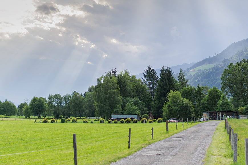 Sunbeams over green meadow and gravel road in mountains