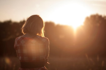 Woman in plaid shirt gazing at sunset in a field