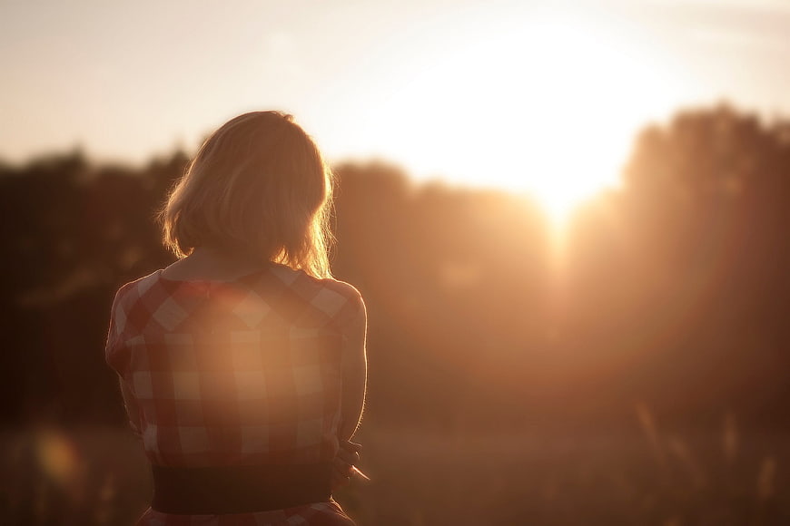 Woman in plaid shirt gazing at sunset in a field