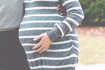 Pregnant woman and partner holding belly in striped sweater