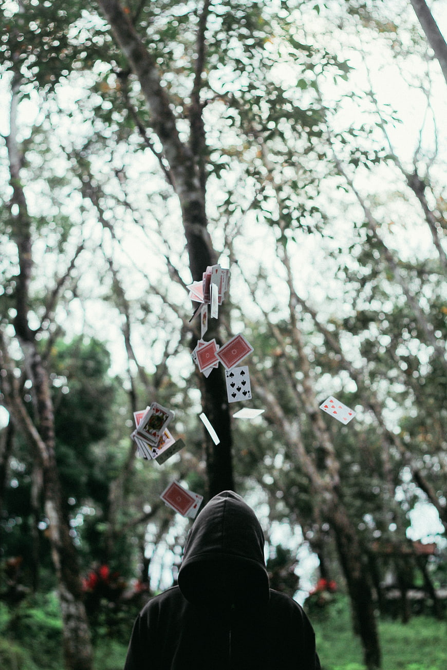 Hooded figure tossing playing cards in a forest