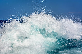 Powerful ocean wave crashing with white foam against blue sky