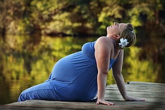 Pregnant woman in blue dress doing yoga on wooden dock