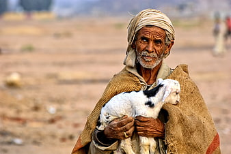 Bedouin man holding a young goat in the desert