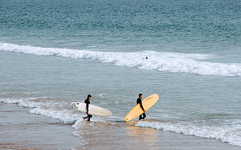 Two surfers walking into ocean waves with boards