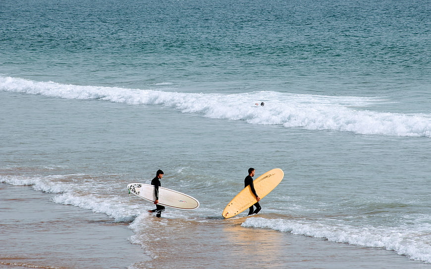 Two surfers walking into ocean waves with boards