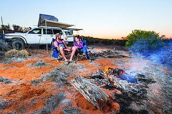 Couple camping by campfire in Australian outback at sunset