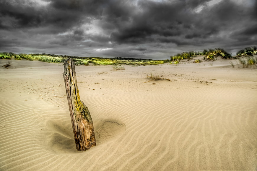 Weathered wooden post in rippled sand dunes under stormy sky