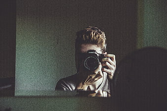 Man taking mirror selfie with DSLR camera in dim room