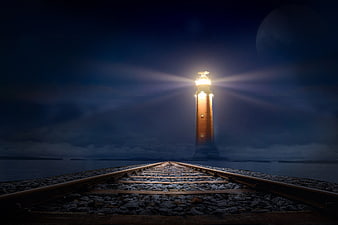 Lighthouse Illuminating Night Sky Over Railway Tracks Leading To Sea