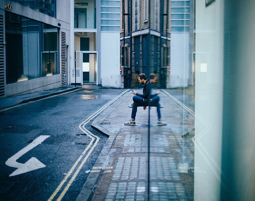 Man sitting on wet city street looking at smartphone