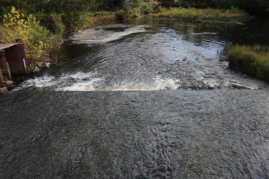 Flowing River with Small Dam and Lush Green Banks