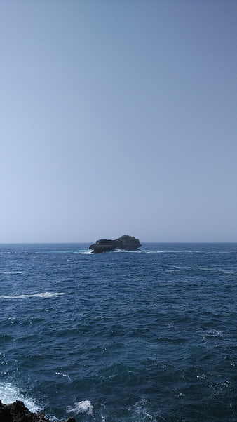 Small rocky island in the ocean with blue sky