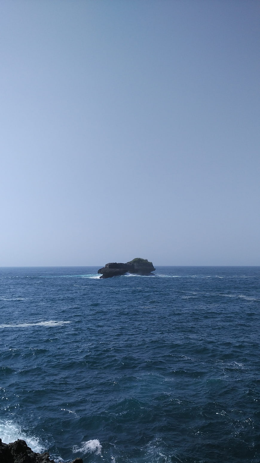 Small rocky island in the ocean with blue sky