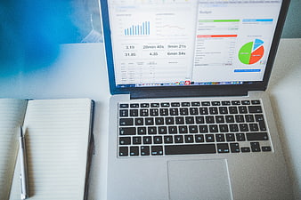 Laptop with financial charts and notebook on desk