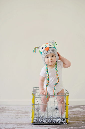 Cute Baby in Crochet Owl Hat Standing in Wire Basket