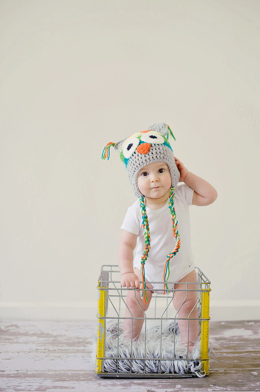 Cute Baby in Crochet Owl Hat Standing in Wire Basket